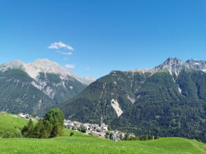 Vue sur le village de Sent depuis le sentier de randonnée, avec la chaîne de montagnes de la Basse-Engadine en arrière-plan.