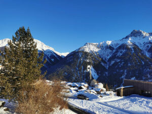 Die Aussicht vom Ferienhaus Chasa Spadla in Sent ist auch im Winter atemberaubend. Im Vordergrund Schulhaus, dann Dorf mit Kirche und dahinter ein einmaliges Bergpanorama
